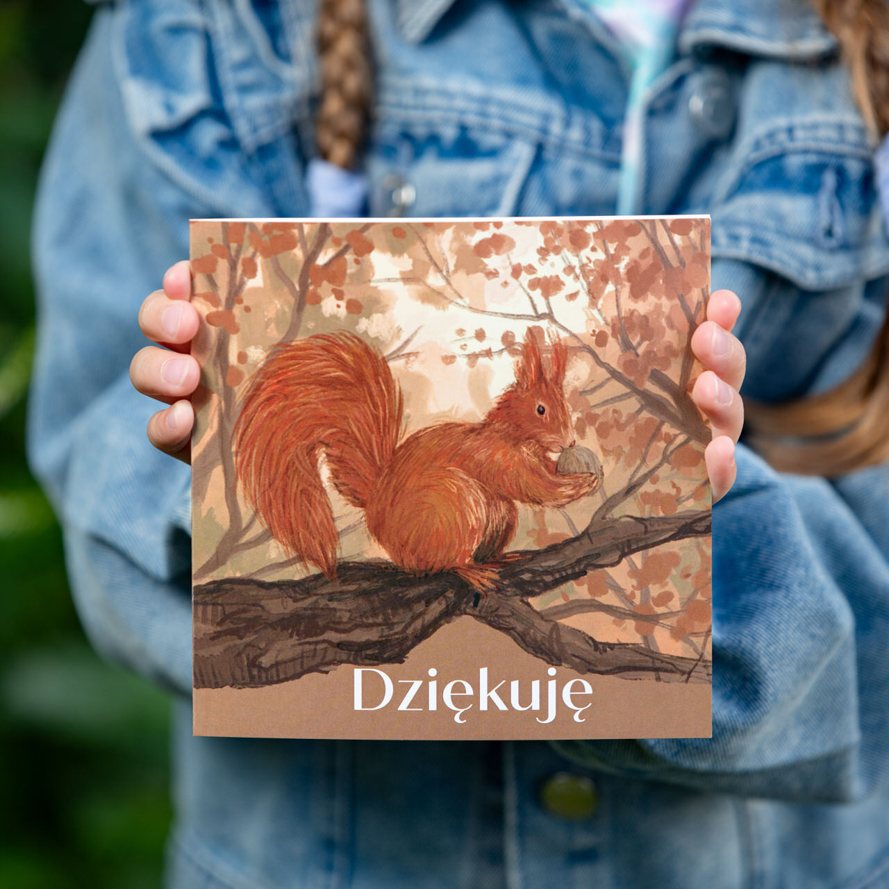 Kartka okolicznościowa, polska firma, z napisem "Dziękuję", na ilustracji wiewiórka pospolita na drzewie, wśród liści. Kartka kwadratowa.
