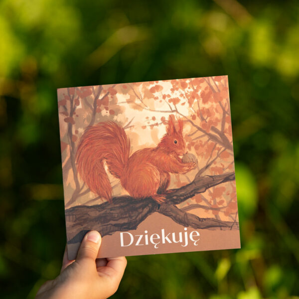 Kartka okolicznościowa z napisem Dziękuję, przyrodnicza, z motywem natury, lasu, drzew i wiewiórką pospolitą. Kartka pokazana na tle polskiej łąki.