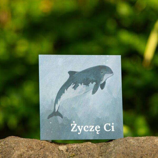 Kartka okolicznościowa, polska produkcja, ekologiczny druk, z motywem przyrody. Kartka na tle lasu, na ilustracji morświn zwyczajny. Napis na kartce "Życzę Ci".