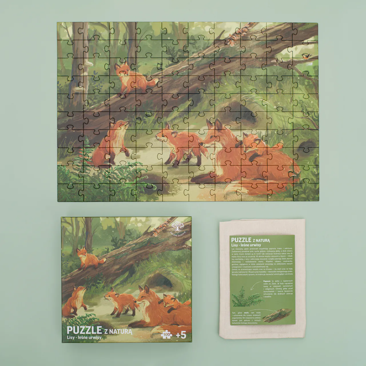 Zielone Złożone Puzzle z naturą Lisy leśne urwisy. Zdjęcie przedstawia co zawiera zestaw tj.: ilustrowane, przyrodnicze puzzle, woreczek bawełniany oraz ulotkę edukacyjną z ciekawostkami przyrodniczymi dotyczącymi fauny i flory z Polski, która została przedstawiona na puzzlach.
