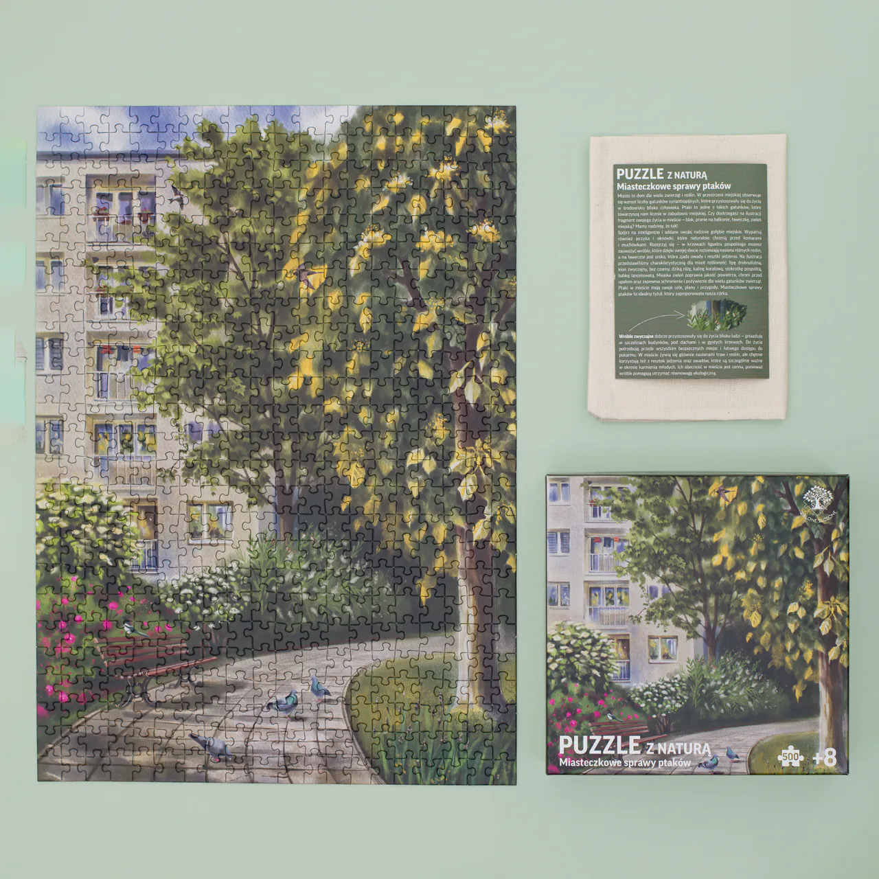 Zielone Złożone Puzzle z naturą Miasteczkowe sprawy ptaków. Zdjęcie przedstawia co zawiera zestaw tj.: ilustrowane, przyrodnicze puzzle, woreczek bawełniany oraz ulotkę edukacyjną z ciekawostkami przyrodniczymi dotyczącymi fauny i flory z Polski, która została przedstawiona na puzzlach.