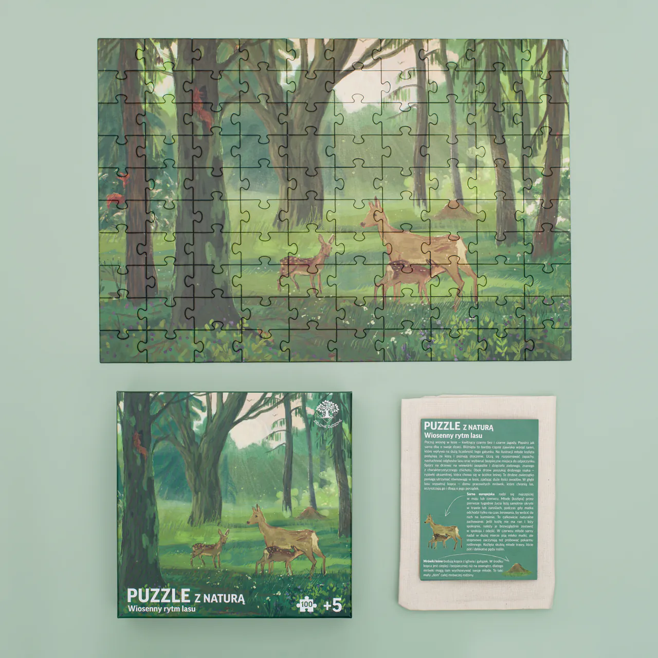Zielone Złożone Puzzle z naturą Wiosenny rytm lasu. Zdjęcie przedstawia co zawiera zestaw tj.: ilustrowane, przyrodnicze puzzle, woreczek bawełniany oraz ulotkę edukacyjną z ciekawostkami przyrodniczymi dotyczącymi fauny i flory z Polski, która została przedstawiona na puzzlach.